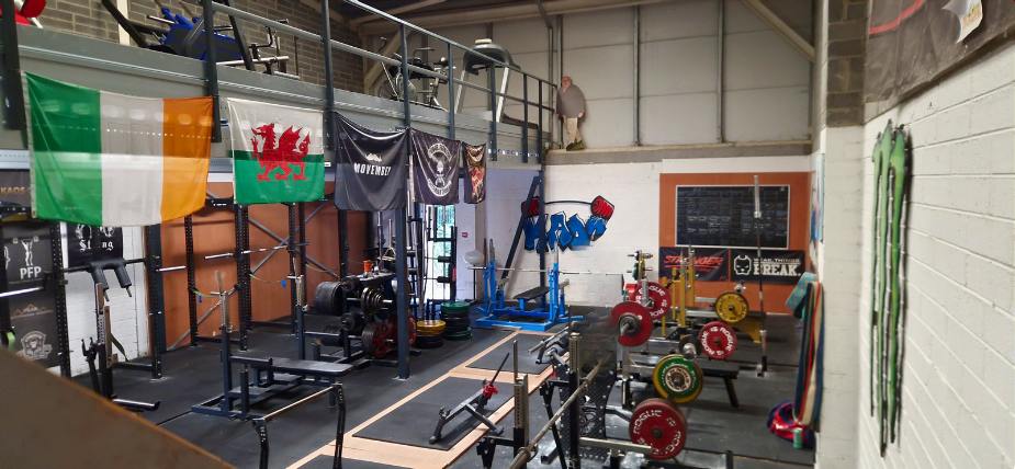 The KAOS gym floor: combo racks, benches and calibrated plates under the flags